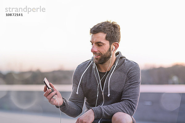 Mittelgroßer erwachsener Mann  im Freien  Smartphone anschauend  Kopfhörer tragend