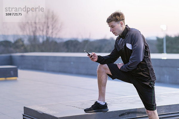 Junger Mann  trägt Sportkleidung  schaut auf Smartphone