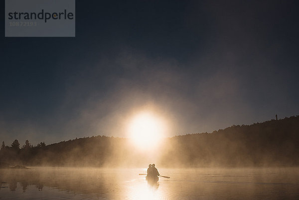 Älteres Ehepaar paddelt bei Sonnenuntergang auf dem See