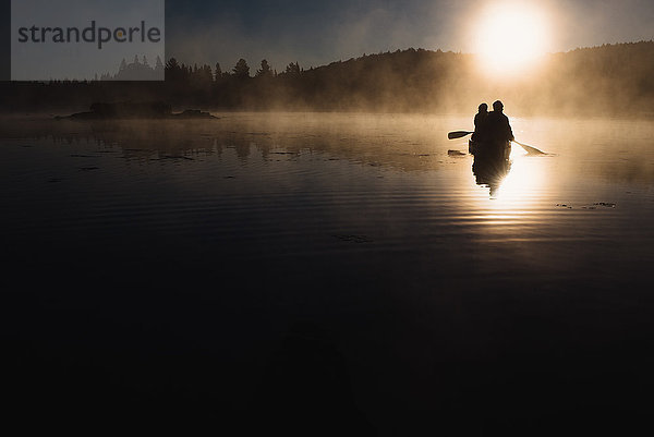 Älteres Ehepaar beim Kanufahren auf dem See bei Sonnenuntergang