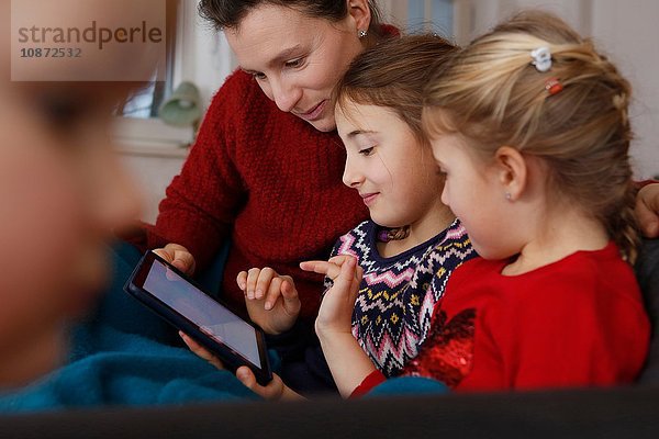 Mutter und Töchter auf dem Sofa sitzend mit digitalem Tablet lächelnd