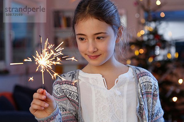 Mädchen vor dem Weihnachtsbaum mit einer Wunderkerze in der Hand schauen lächelnd nach unten