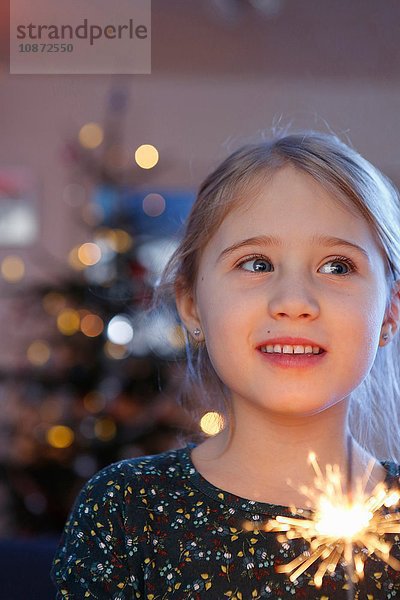 Mädchen vor dem Weihnachtsbaum  die eine Wunderkerze halten und lächelnd wegschauen