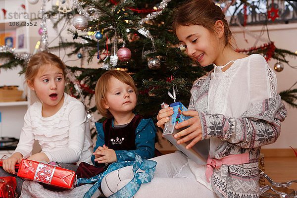 Mädchen vor dem Weihnachtsbaum beim Öffnen von Geschenken