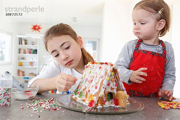 Schwestern an der Küchentheke beim Dekorieren des Lebkuchenhauses