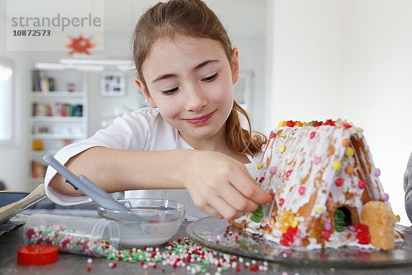 Mädchen an Küchentheke schmückt Lebkuchenhaus lächelnd