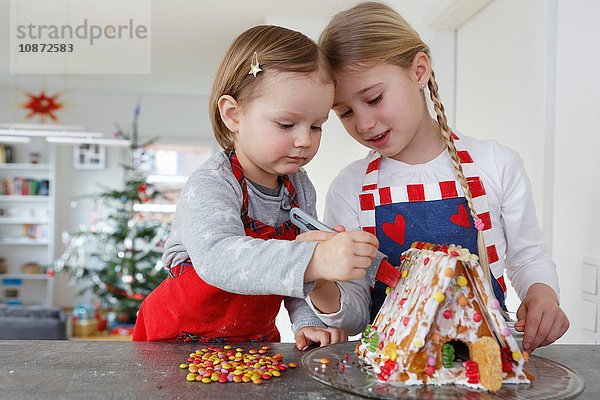 Mädchen an der Küchentheke schmücken gemeinsam das Lebkuchenhaus