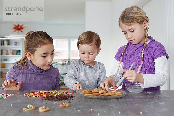 Mädchen am Küchentisch beim Dekorieren von Keksen