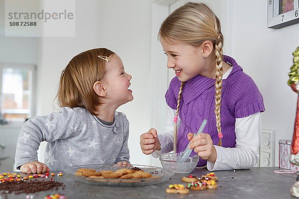 Mädchen an der Küchentheke dekorieren Kekse von Angesicht zu Angesicht lächelnd
