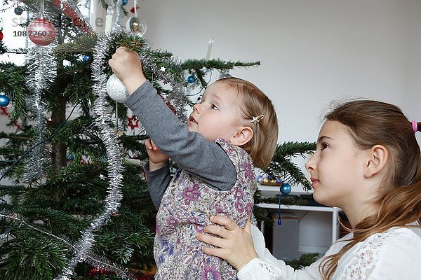 Seitenansicht der großen Schwester hilft Mädchen beim Schmücken des Weihnachtsbaums