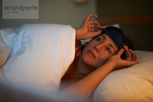 Reife Frau setzt nachts im Hotelbett eine Augenmaske auf