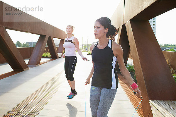 Zwei Frauen trainieren mit Springseilen auf städtischer Fußgängerbrücke