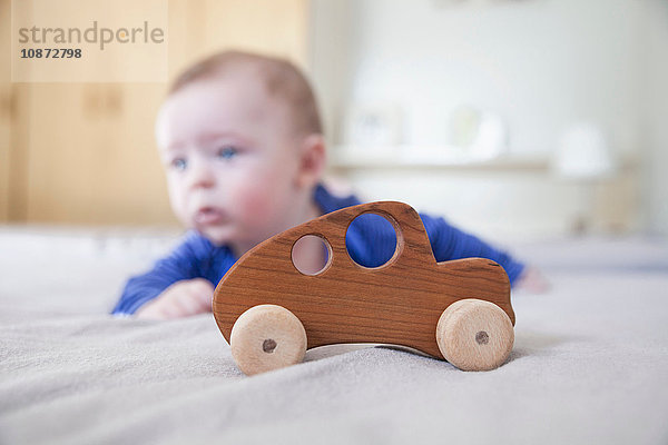 Kleiner Junge spielt auf dem Bett mit Holzspielzeugauto