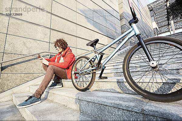 Mann sitzt auf Stufen mit BMX mit Smartphone