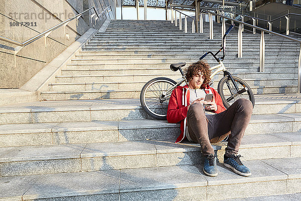 Mann sitzt auf Stufen mit BMX mit Smartphone