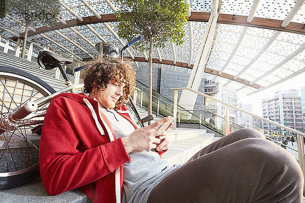 Mann sitzt auf einer Treppe mit BMX über Smartphone