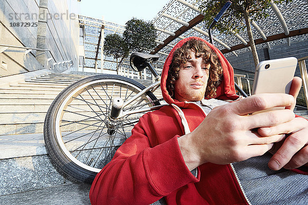 Mann sitzt auf einer Treppe mit BMX über Smartphone