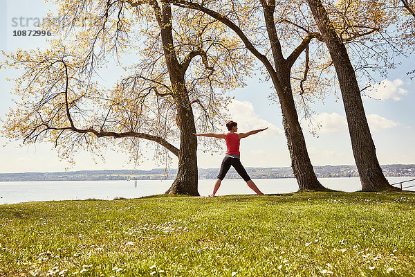 Rückansicht einer Frau  die am See Yoga praktiziert