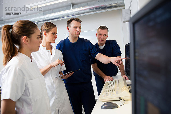 Ärzte und Krankenschwestern zeigen im CT-Kontrollraum auf Röntgenbilder auf dem Monitor