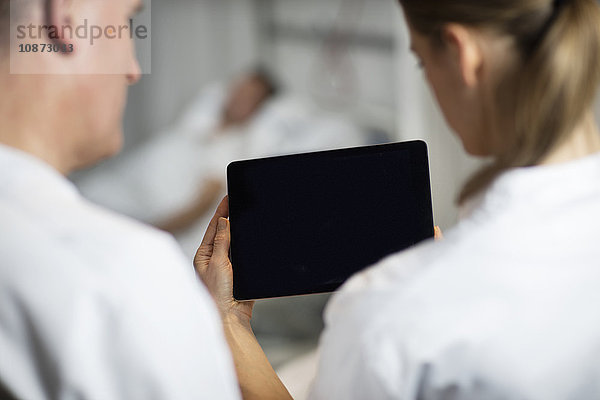 Über-Schulter-Ansicht von Ärzten  die sich ein Fuß-Röntgenbild auf einem digitalen Tablett auf der Krankenhausstation ansehen