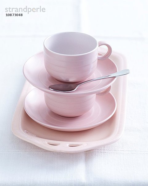 Rosa Tassen und Untertassen auf Teller gestapelt  die für hohen Tee vorbereitet werden