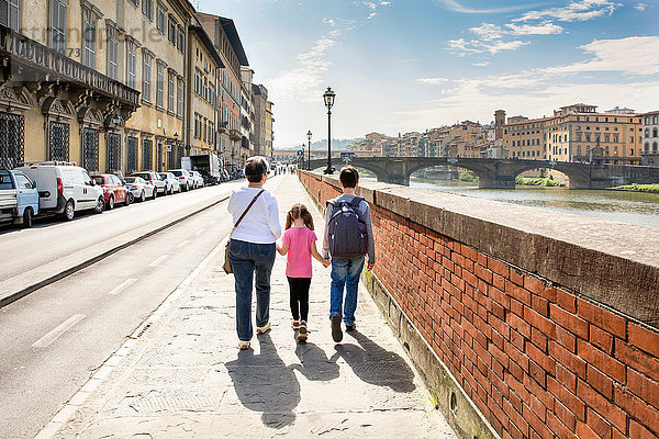 Rückansicht einer älteren Frau und zweier Enkelkinder beim Spaziergang am Arno  Florenz  Italien