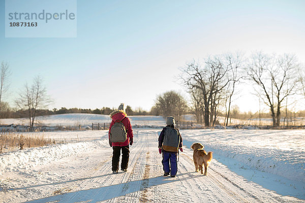 Golden Retriever und zwei junge Schwestern mit Schulranzen auf verschneiter Piste  Ontario  Kanada