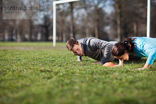 Junge Frau und Mann machen Push-Ups auf dem Spielfeld