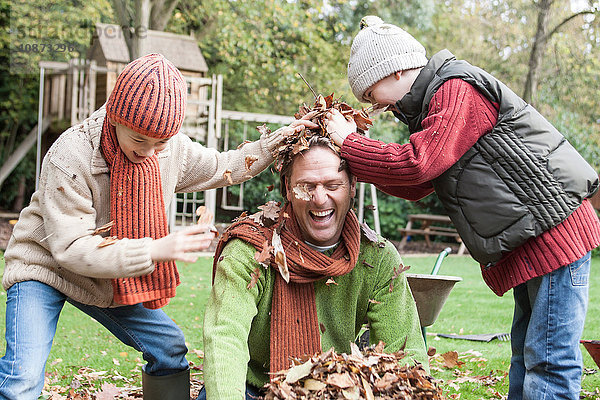 Vater und Söhne treiben sich im Garten herum und werfen Herbstblätter