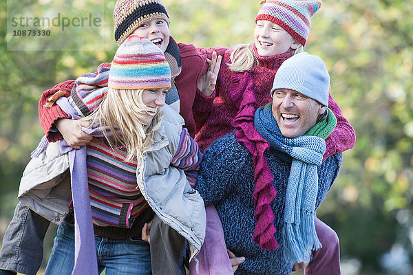 Familie gemeinsam im Park  Mutter und Vater tragen Kinder auf dem Rücken  lachend