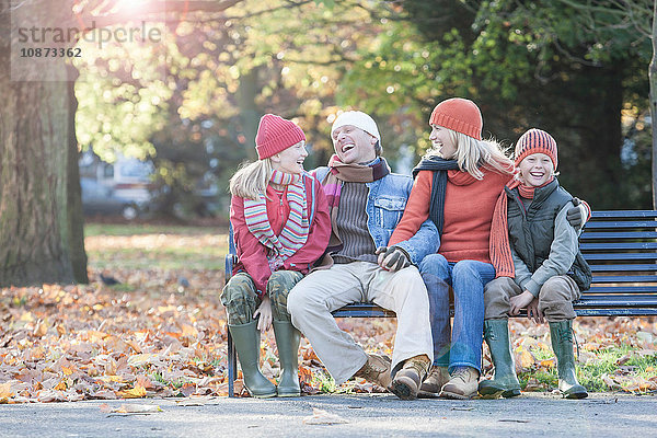 Familie sitzt zusammen auf der Parkbank und lacht