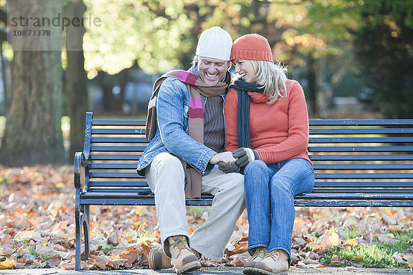 Heterosexuelles Paar sitzt zusammen auf einer Parkbank  hält Händchen und lacht