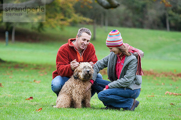 Heterosexuelles Paar im Park  kauernder  streichelnder Hund