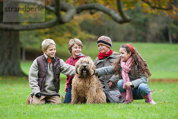 Vier Kinder im Park  kauernder  streichelnder Hund