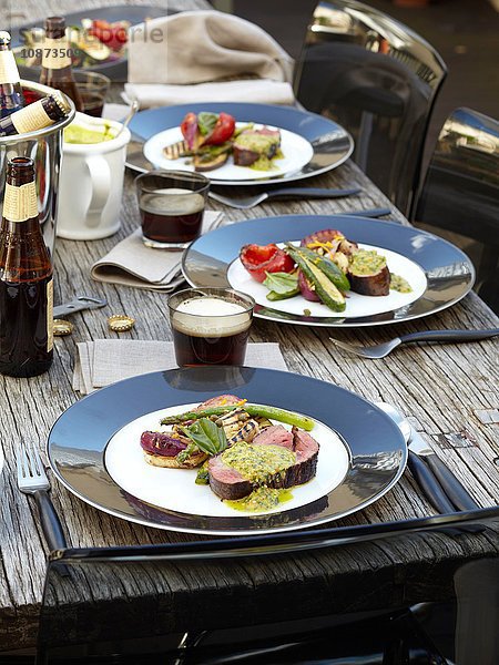 Hochwinkelansicht von Chimichurri-Rindfleisch mit gegrilltem Salat im Freien auf einem hölzernen Gartentisch