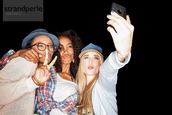 Junge Frauen drängten sich zusammen  machten Friedenszeichen  spitzten die Lippen  benutzten das Smartphone  um sich selbst zu erobern