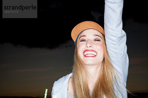 Junge Frau mit Baseballcap und erhobenem Arm schaut lächelnd weg