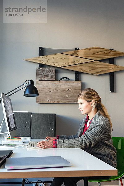 Seitenansicht einer jungen Frau im Büro  die am Schreibtisch am Computer sitzt