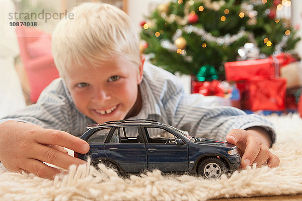 Junge liegt vorne und hält ein Spielzeugauto  schaut lächelnd in die Kamera