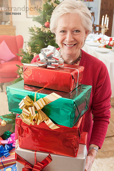 Frau hält Stapel Weihnachtsgeschenke in der Hand und schaut lächelnd in die Kamera