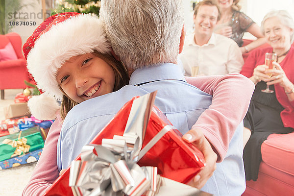 Enkelin hält Weihnachtsgeschenk und umarmt Großvater lächelnd