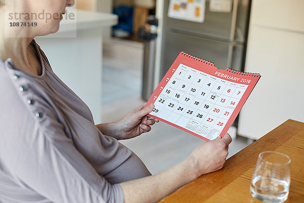 Hochwinkel-Seitenansicht einer schwangeren Frau beim Blick auf den Kalender