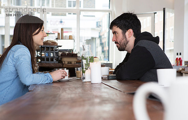 Mittelgroßes erwachsenes Paar sitzt am Café-Tisch bei Kaffee und unterhält sich