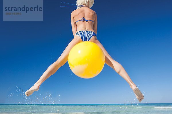 Rückansicht einer jungen Frau  die auf einem Raumtrichter am Strand in die Luft springt  Mallorca  Spanien