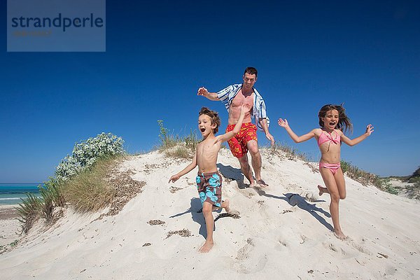 Mittelgroßer erwachsener Mann rennt auf Sanddüne mit Sohn und Tochter am Strand  Mallorca  Spanien