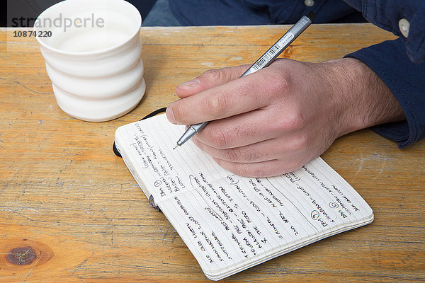 Hand eines Mannes am Cafétisch schreibt in Notizbuch