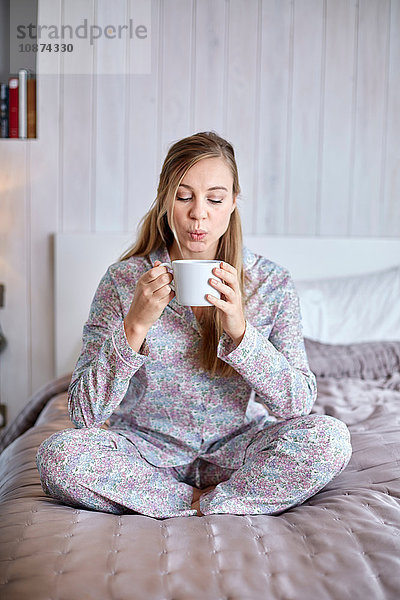 Frau im Pyjama trinkt Kaffee im Bett