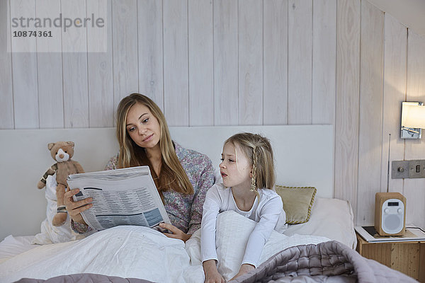 Mutter liest Zeitung neben Tochter im Bett