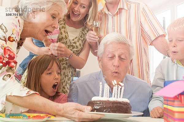 Mann umringt von Familie bläst Kerze auf Geburtstagskuchen aus