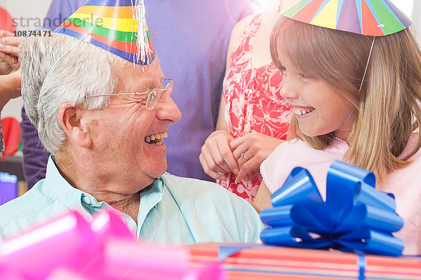 Großvater und Enkelin tragen Partyhüte von Angesicht zu Angesicht lächelnd